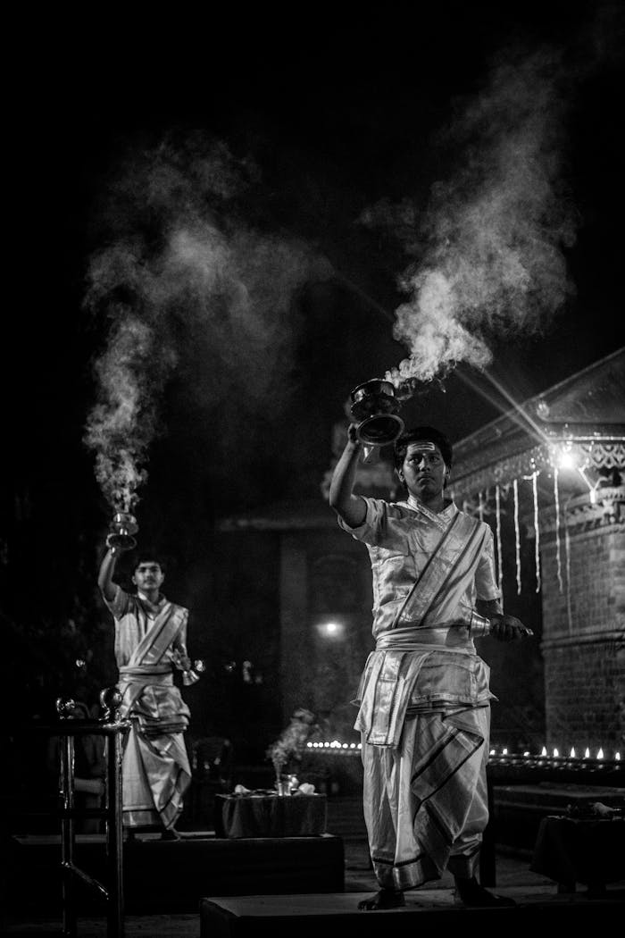 Black and white photo of men performing a traditional Indian prayer ritual at night with incense.